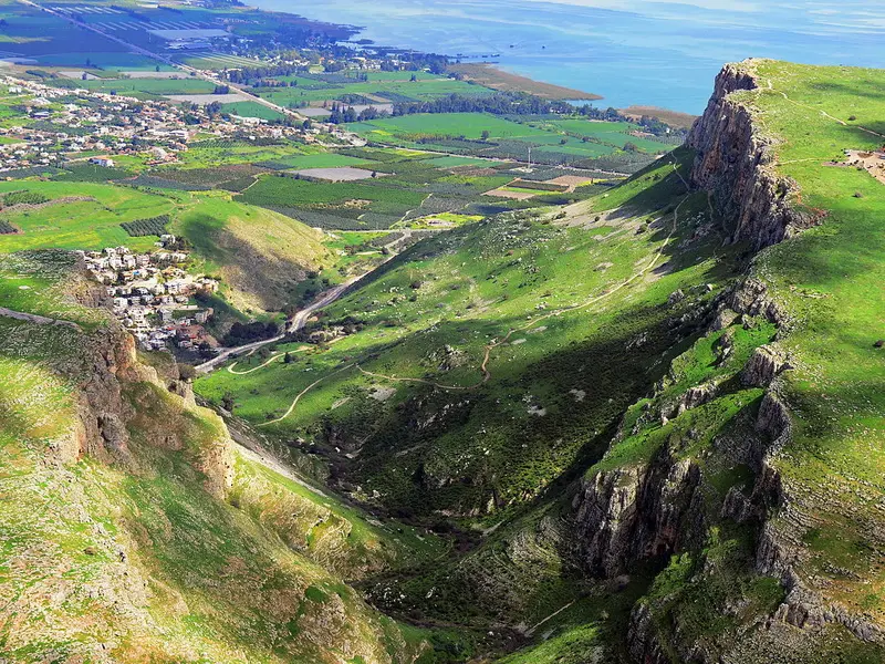 The cliff of Mount Arbel rising above green fields and the Sea of Galilee