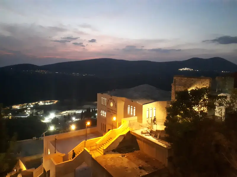 Lights coming on over the old city of Tzfat at dusk, with the Galilee hills beyond